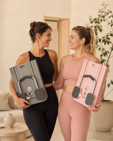 Twee vrouwen die naar elkaar lachen een samen een plexis pilates board vasthouden